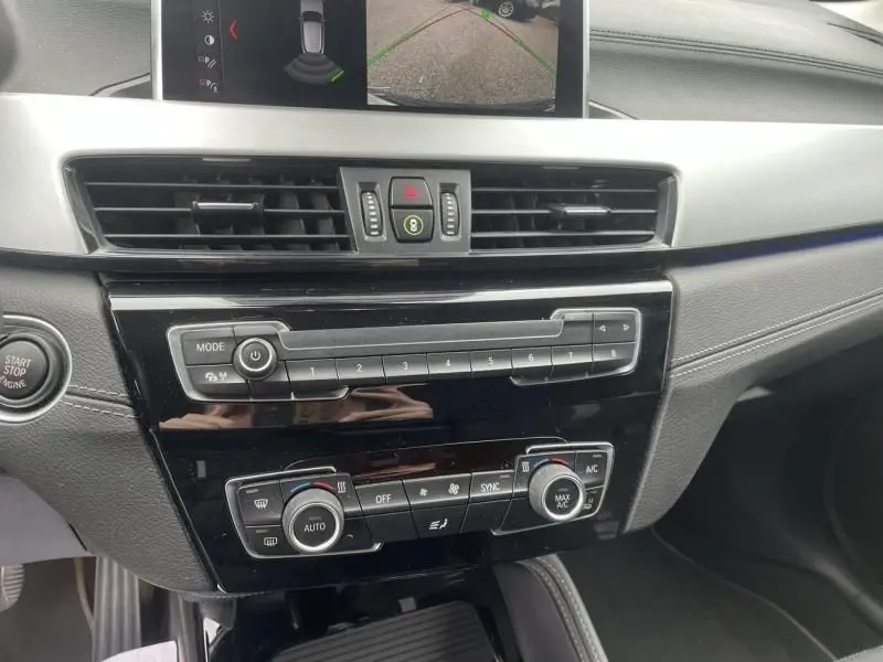 Vue intérieure du tableau de bord du BMW X2 bleu métal 2021, avec écran de caméra de recul et commandes climatisation visibles.
