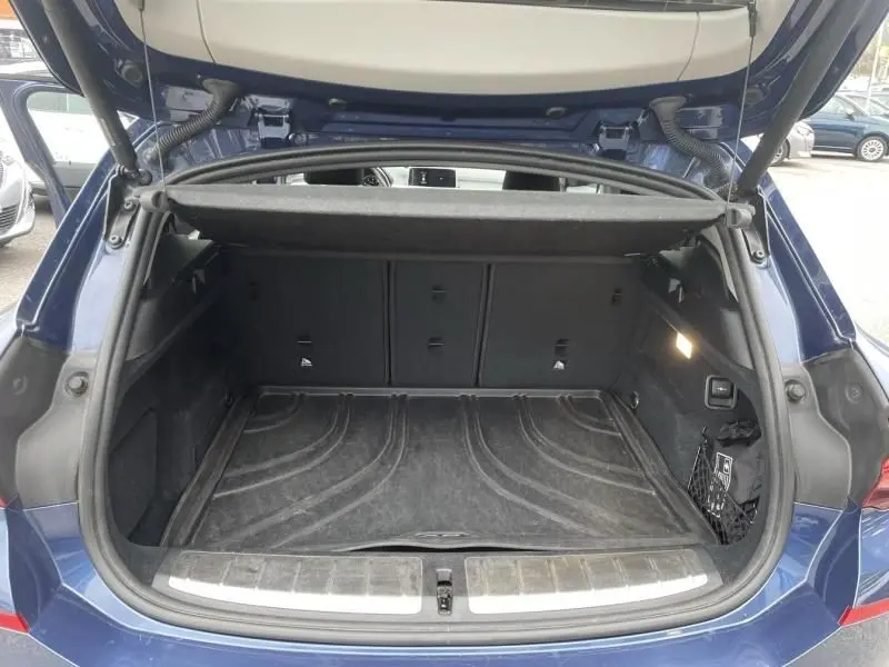 Coffre ouvert vu de l'arrière d'un BMW X2 bleu métal 2021, montrant l'espace de chargement et la moquette noire.