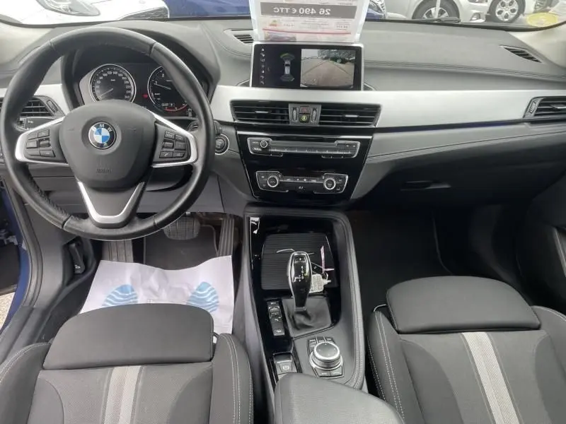 Vue intérieure du poste de conduite du BMW X2 bleu métal 2021, avec volant multifonction, écran central et levier de boîte automatique.