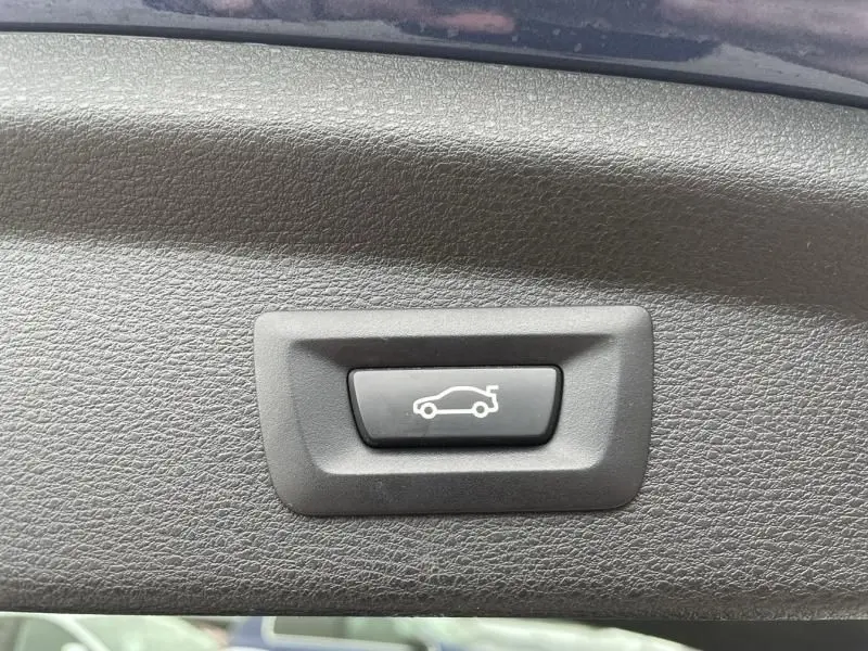 Bouton d'ouverture électrique du coffre sur la garniture intérieure d'un BMW X2 bleu métal, version Lounge 2021.