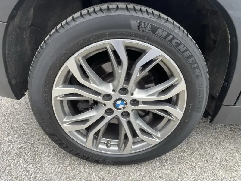 Gros plan sur la roue avant droite d’une BMW X2 bleu métal, jante alliage à design étoilé et pneu Michelin.