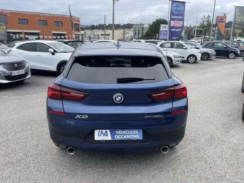 Vue arrière d'une BMW X2 bleu métal X-Drive 20 da 190 cv, avec feux rouges et double sortie d'échappement visible.
