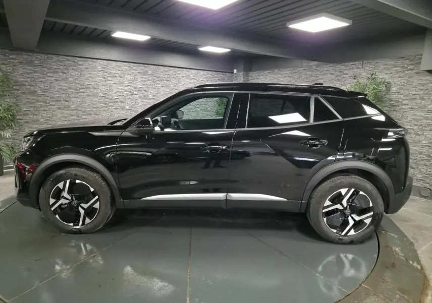 Profil côté gauche du Peugeot 2008 noir brillant avec jantes alliage bi-ton dans un showroom intérieur.