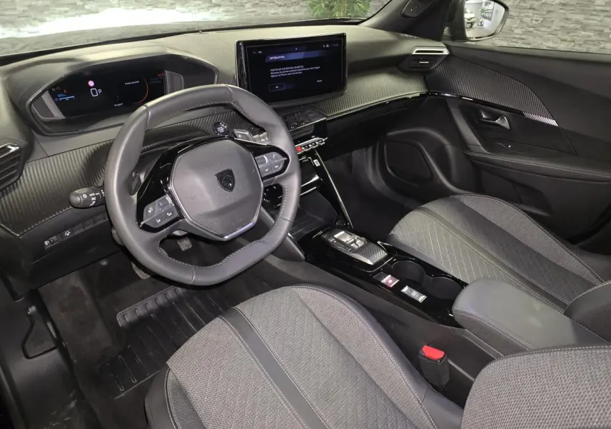 Intérieur avant du Peugeot 2008 noir 2025, tableau de bord carbone, volant compact et écran tactile central.