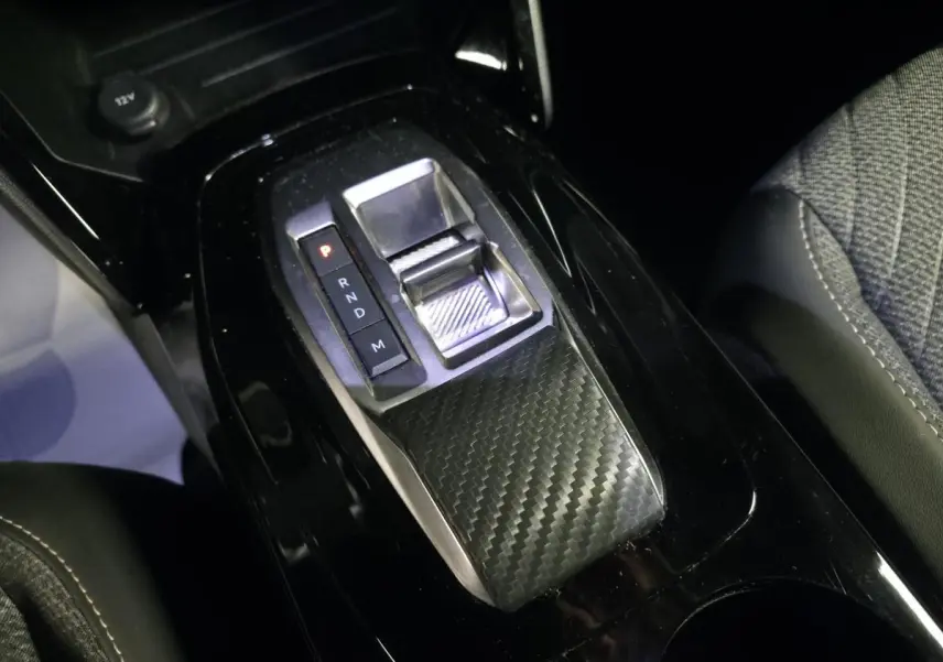 Gros plan sur la console centrale noire brillante du Peugeot 2008 1.2i Hybrid avec sélecteur de boîte automatique en carbone.
