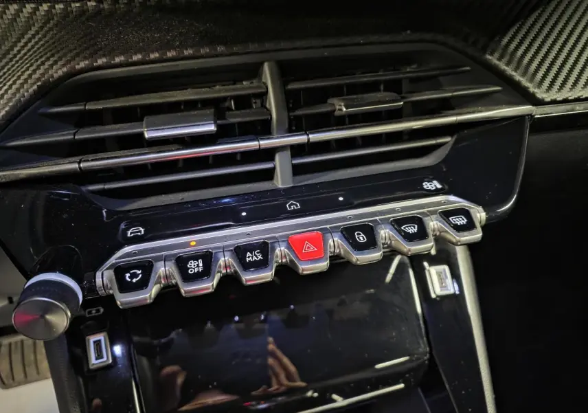 Gros plan sur la console centrale du Peugeot 2008 noir 2025, avec boutons de commande et décor carbone.