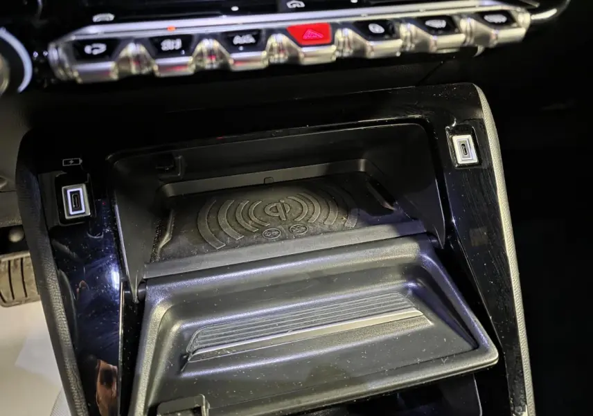 Gros plan sur la console centrale noire du Peugeot 2008 2025 avec zone de recharge sans fil et ports USB.