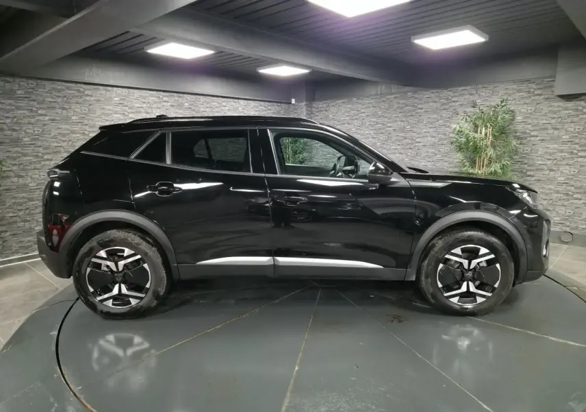 Vue latérale droite d’un Peugeot 2008 noir brillant avec jantes alliage bi-ton et barres de toit noires.