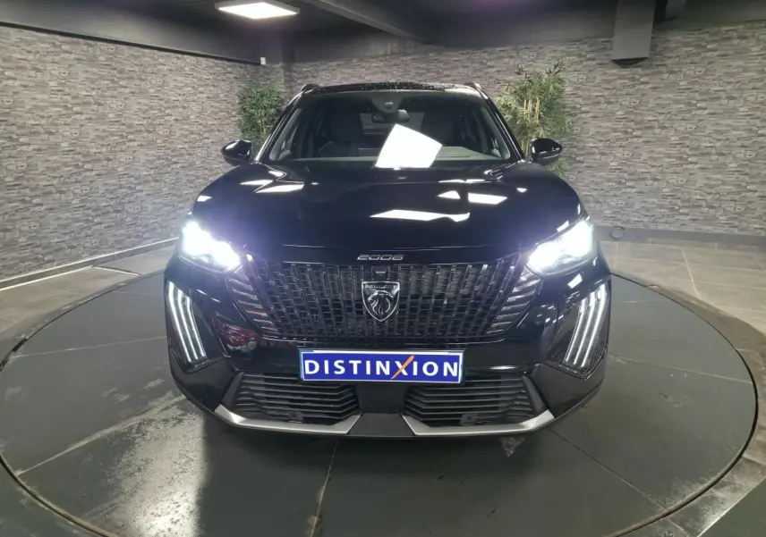 Vue frontale d'un Peugeot 2008 noir avec feux allumés et calandre noire à l'intérieur moderne.