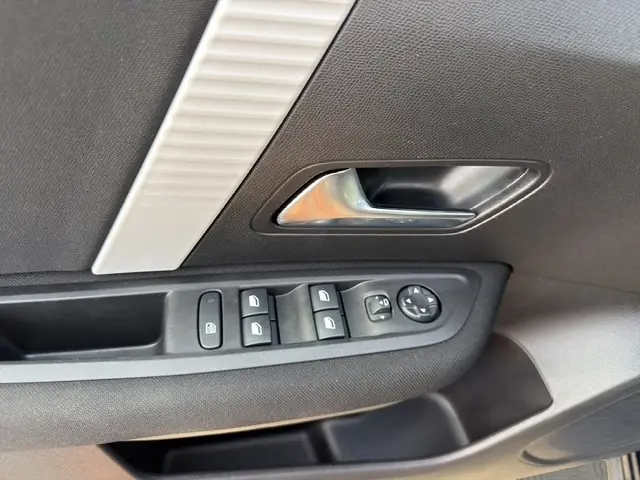 Gros plan sur la commande des vitres et poignée intérieure côté conducteur d'une Citroën C4 hybride bleue 2025.