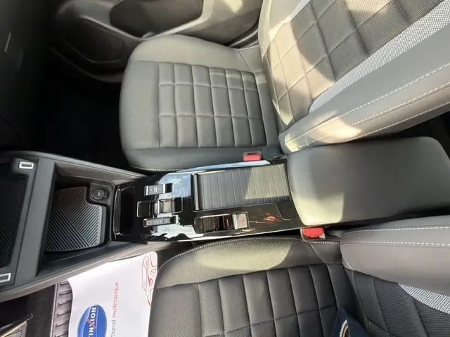 Vue plongeante sur la console centrale noire et les sièges tissu gris foncé du Citroën C4 hybride 2025.