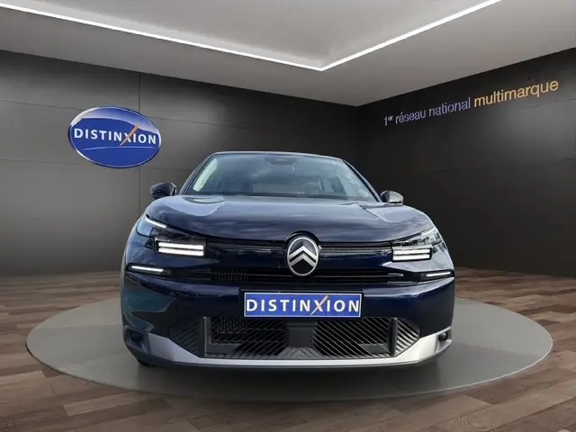Vue frontale d'une Citroën C4 hybride bleu foncé, avec logo distinctif et éclairage LED moderne en showroom.