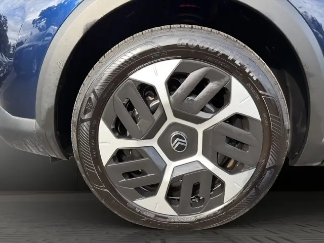 Gros plan sur la roue avant droite d'une Citroën C4 hybride bleue 2025 avec jante au design moderne bicolore.