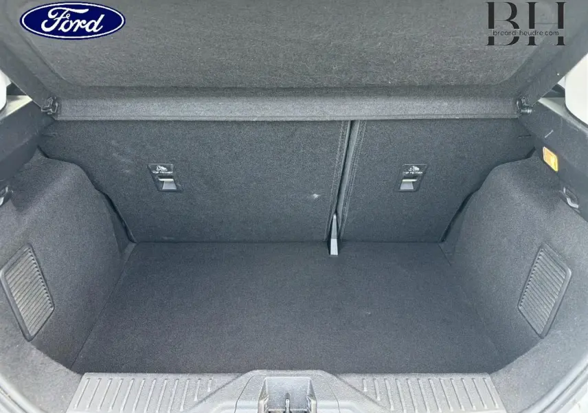 Coffre ouvert d'une Ford Fiesta blanc glacier, vue de l'intérieur montrant l'espace de chargement et la banquette arrière rabattable.