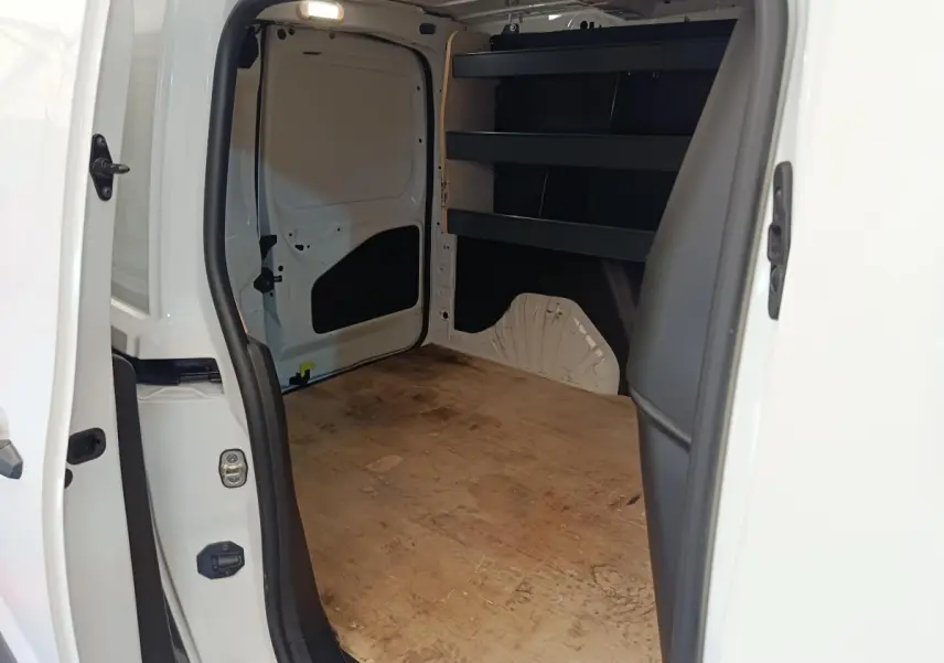 Vue intérieure arrière du Citroën Berlingo blanc, montrant l’espace de chargement avec étagères noires et plancher en bois.