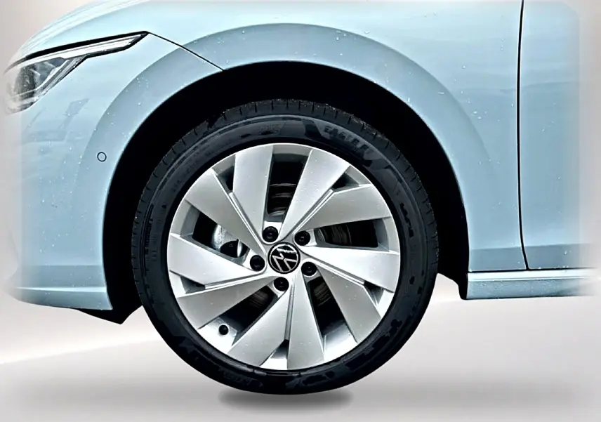 Gros plan sur la roue avant gauche d’une Volkswagen Golf bleu glacier avec jante alu 17 pouces et phare avant partiel visible.