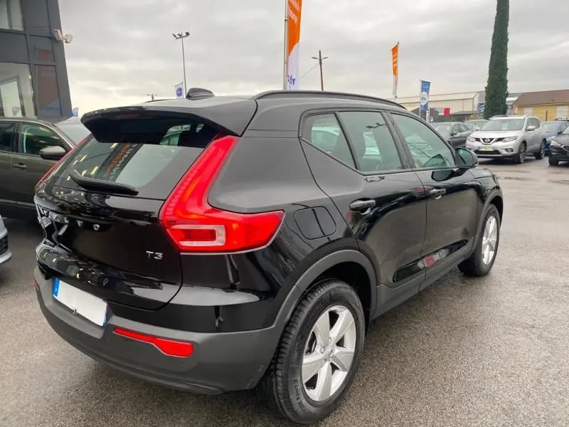 Vue 3/4 arrière droite d'un Volvo XC40 T3 noir solid avec feux arrière en forme de L et jantes argentées.