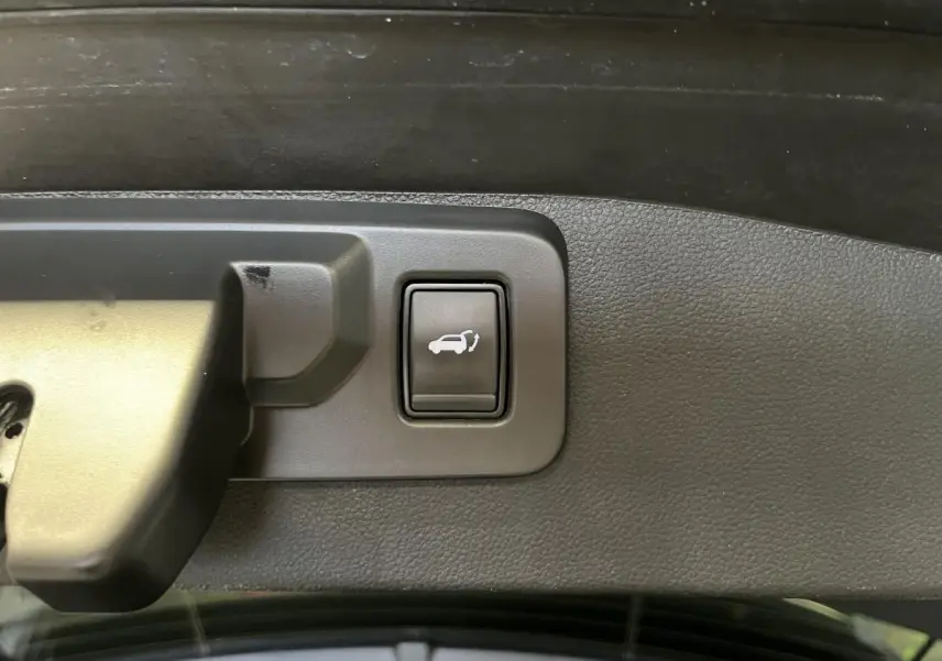 Bouton d'ouverture électrique du hayon sur le panneau intérieur du coffre du Renault Austral gris 2024.