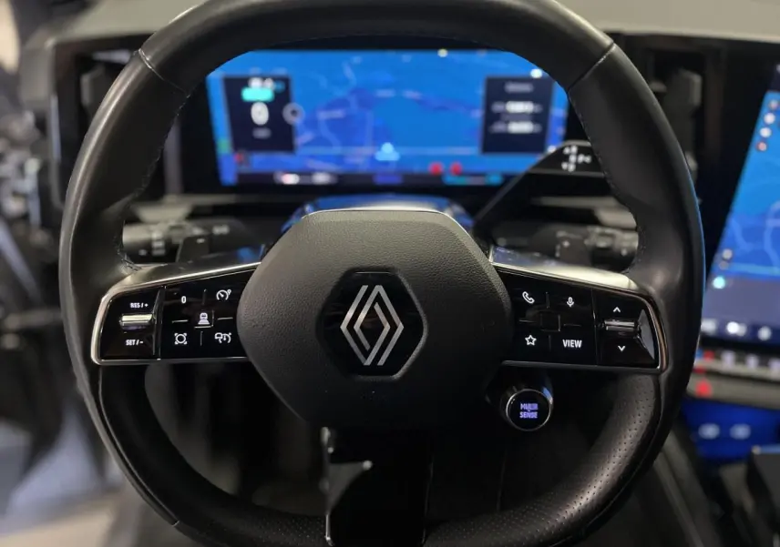 Vue rapprochée du volant noir de Renault Austral 2024 avec commandes intégrées et tableau de bord numérique lumineux en arrière-plan