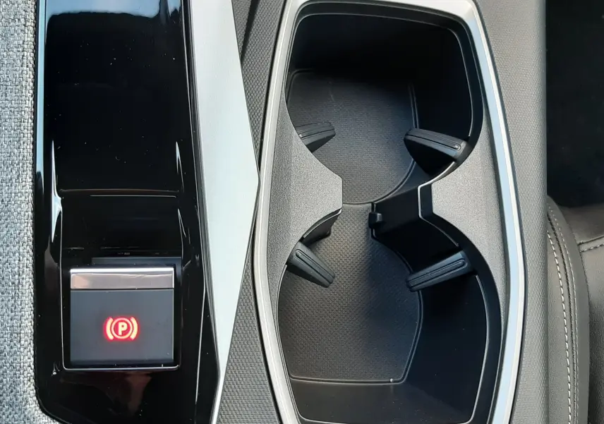 Gros plan sur la console centrale noire et grise avec porte-gobelets et bouton de frein à main électrique du Peugeot 5008 2025.