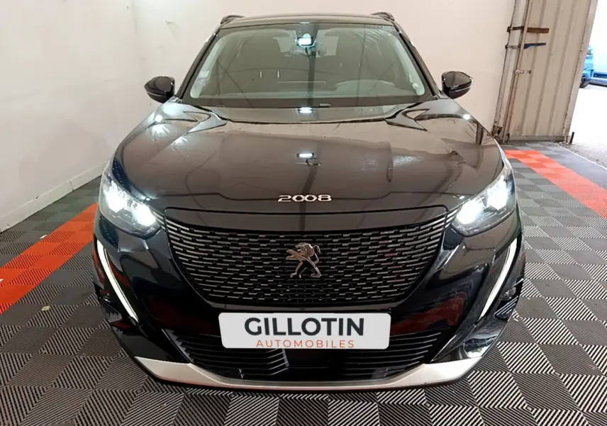 Peugeot 2008 noir vue de face avec phares LED allumés et calandre distinctive dans un garage.