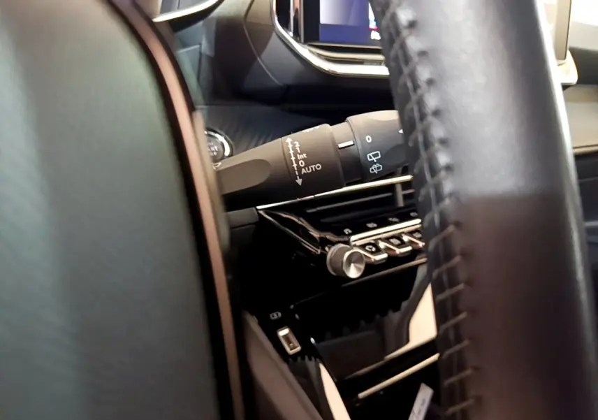 Détail du commodo d’essuie-glace côté gauche et partie du volant cuir dans l’habitacle noir du Peugeot 2008.