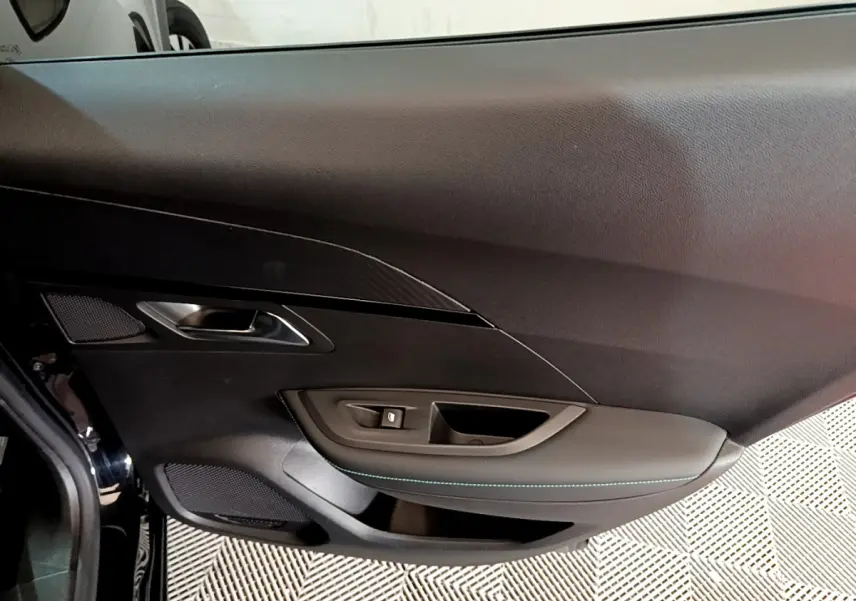 Intérieur côté gauche de la porte d'une Peugeot 2008 noire, avec garniture noire et surpiqûres bleues.