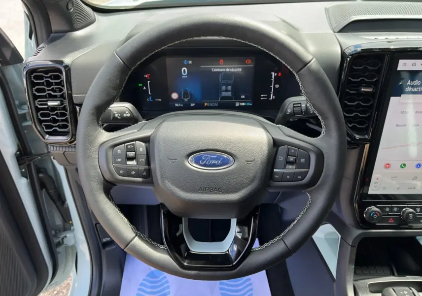 Vue intérieure centrée sur le volant cuir multifonctions du Ford Ranger gris zen avec tableau de bord digital et écran tactile.