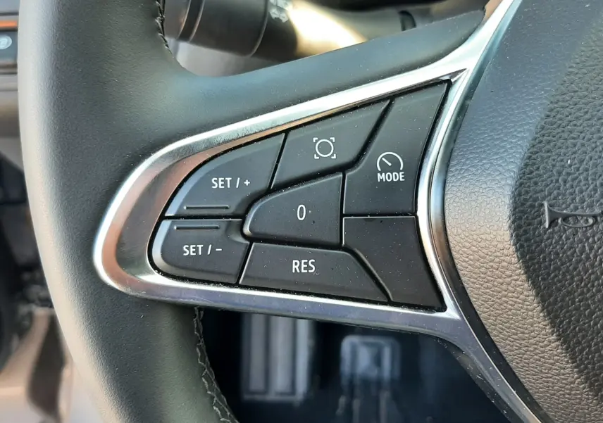 Gros plan sur les commandes à gauche du volant noir du Renault Captur gris Cassiopée, boutons de régulateur et mode visibles.