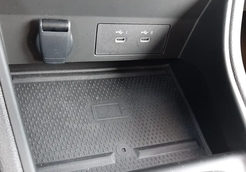 Gros plan sur la console centrale du Renault Captur gris Cassiopée 2025, montrant les ports USB-C et un espace de rangement avec chargeur sans fil.