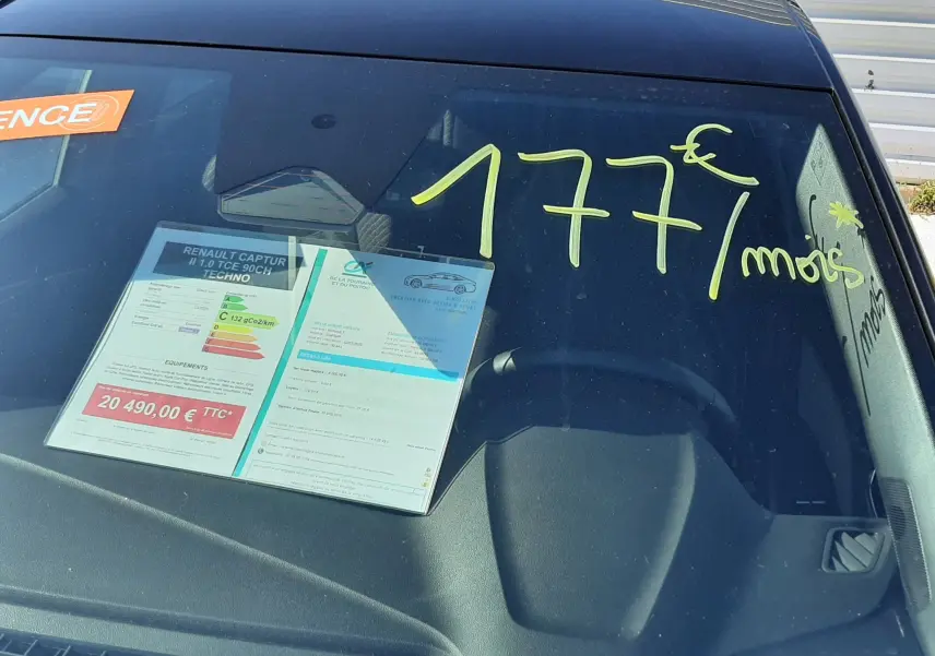 Vue avant rapprochée du Renault Captur gris Cassiopée avec inscription jaune "177€/mois" sur le pare-brise.