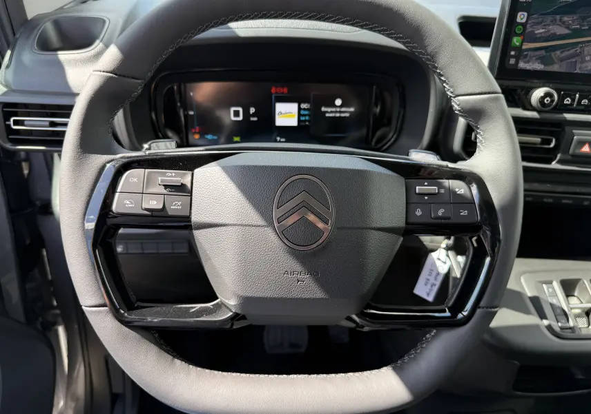 Vue frontale du volant en cuir noir du Citroën Berlingo gris Artense, avec commandes intégrées et tableau de bord numérique.