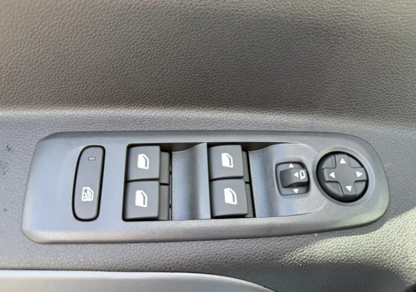 Panneau de commandes des vitres et rétroviseurs côté conducteur du Citroën Berlingo gris Artense, vue rapprochée intérieure.