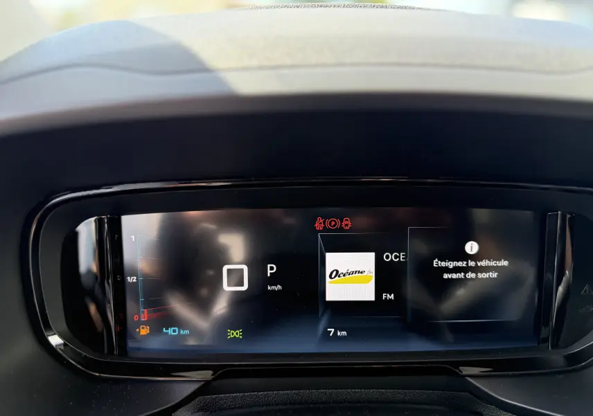 Tableau de bord numérique du Citroën Berlingo 2026 gris, affichant la vitesse, radio et message d’alerte.
