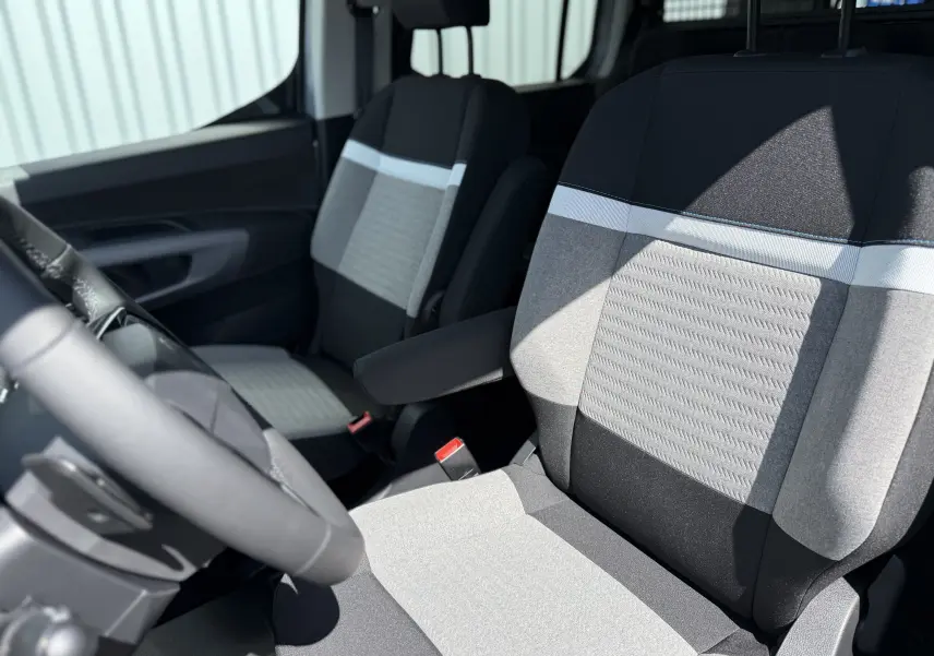 Vue intérieure rapprochée des sièges avant gris clair et noir du Citroën Berlingo 2026, avec accoudoir côté droit.