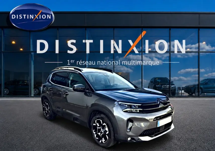 Citroën C5 Aircross gris 3/4 avant droit avec jantes alu et barres de toit devant vitrine Distinxion.