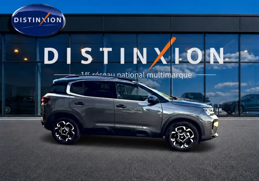 Profil droit du Citroën C5 Aircross gris 2025 avec jantes alu et barres de toit devant vitrine Distinxion.