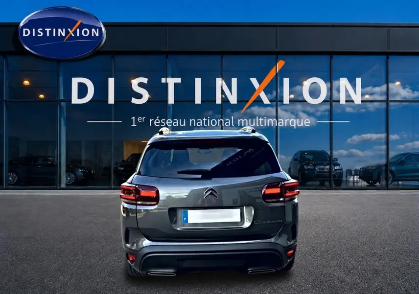 Vue arrière d'un Citroën C5 Aircross gris 2025 stationné devant une vitrine avec logo Distinxion.