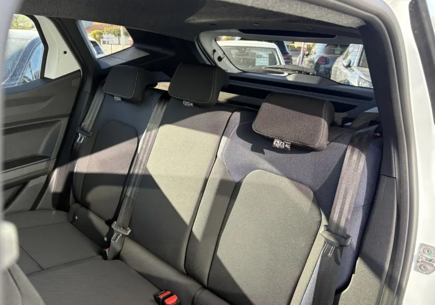 Vue intérieure arrière droite du Dacia Duster 2024 blanc, montrant la banquette arrière en sellerie Denim avec appuie-têtes et ceintures de sécurité.