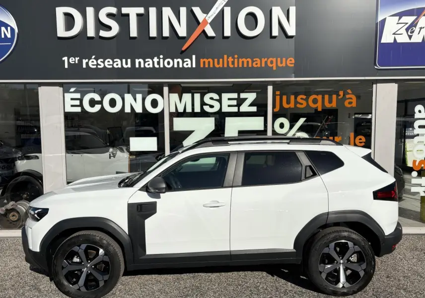 Profil droit du Dacia Duster 2024 blanc métallisé avec jantes alliage noires et barres de toit noires.