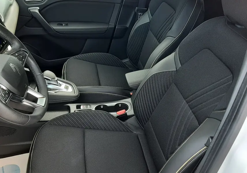 Vue intérieure côté conducteur de la Renault Symbioz E-Tech blanc nacré, sièges noirs en tissu avec surpiqûres contrastées.
