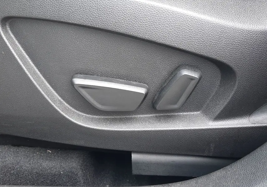 Gros plan sur les commandes électriques de réglage du siège côté gauche dans l’habitacle noir du Renault Symbioz blanc nacré.
