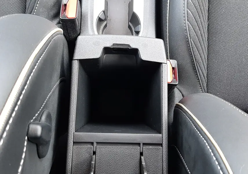 Vue plongeante sur la console centrale noire avec rangement ouvert et sièges tissu noir aux surpiqûres claires du Renault Symbioz 2025.