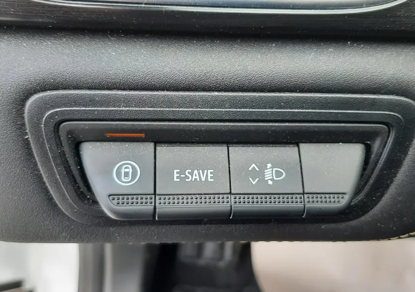 Boutons de commande du mode E-SAVE et réglage des phares dans l'habitacle noir du Renault Symbioz blanc nacré, vue rapprochée.