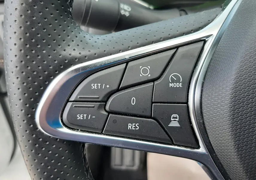 Gros plan sur les commandes noires du volant en cuir perforé du Renault Symbioz blanc nacré, avec boutons de régulateur et mode.