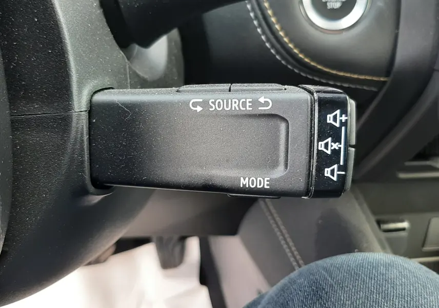 Gros plan sur la commande au volant gauche du Renault Symbioz blanc nacré, avec bouton source et mode visible.