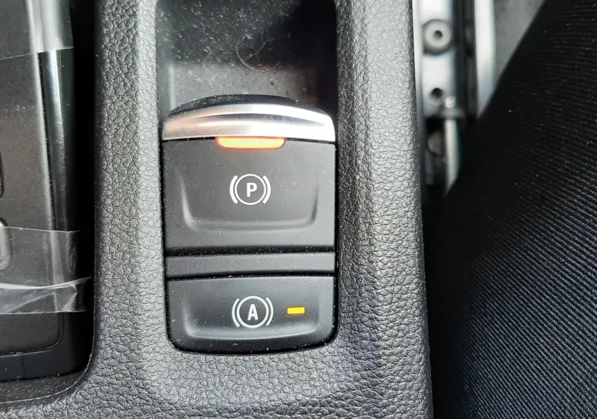 Gros plan sur les commandes de frein à main électronique et arrêt auto dans l’habitacle noir du Renault Symbioz blanc nacré.
