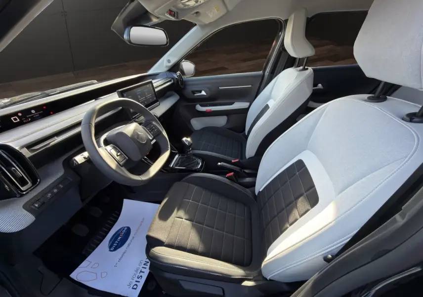 Vue intérieure côté conducteur de la Citroën C3 2025, sièges bicolores gris et noir, tableau de bord avec écran tactile.