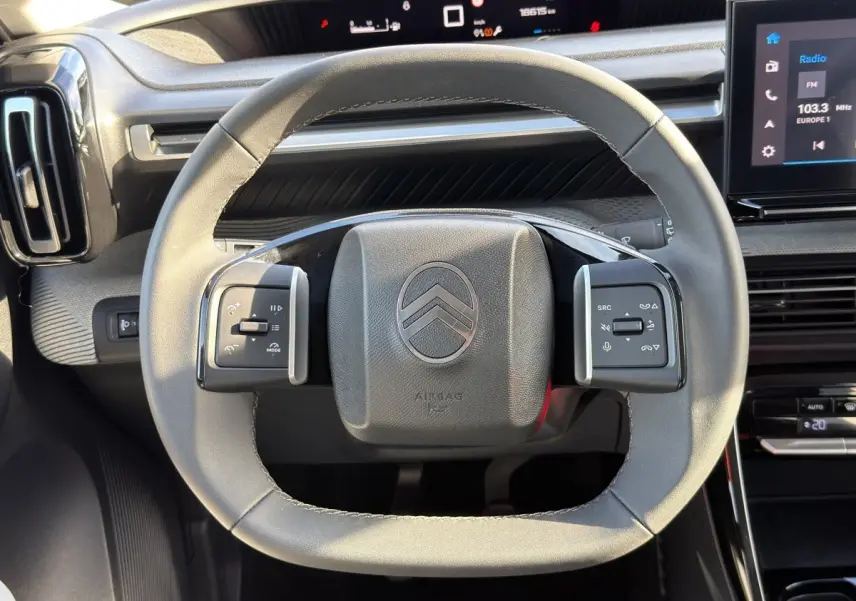 Vue rapprochée du volant cuir gris clair de la Citroën C3 2025 avec commandes multifonctions et tableau de bord numérique.