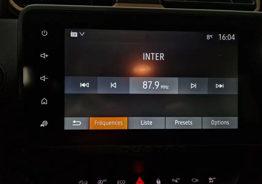 Écran tactile central du tableau de bord du Dacia Duster blanc 2024 affichant la radio FM sur 87.9 MHz à 16h04